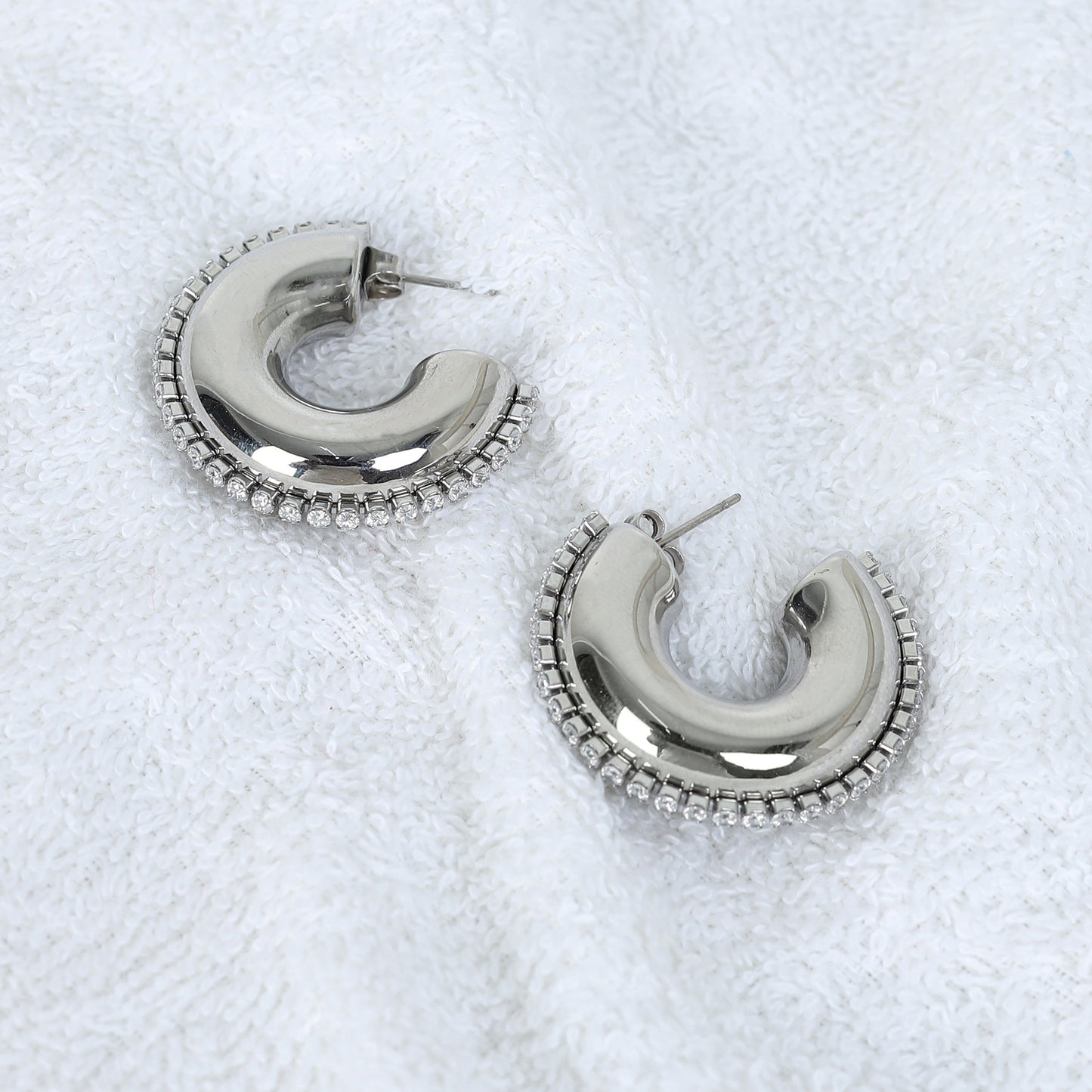 The Half Circle Silver Hoop features a shiny silver finish and a beaded edge design, beautifully showcased on textured white fabric.