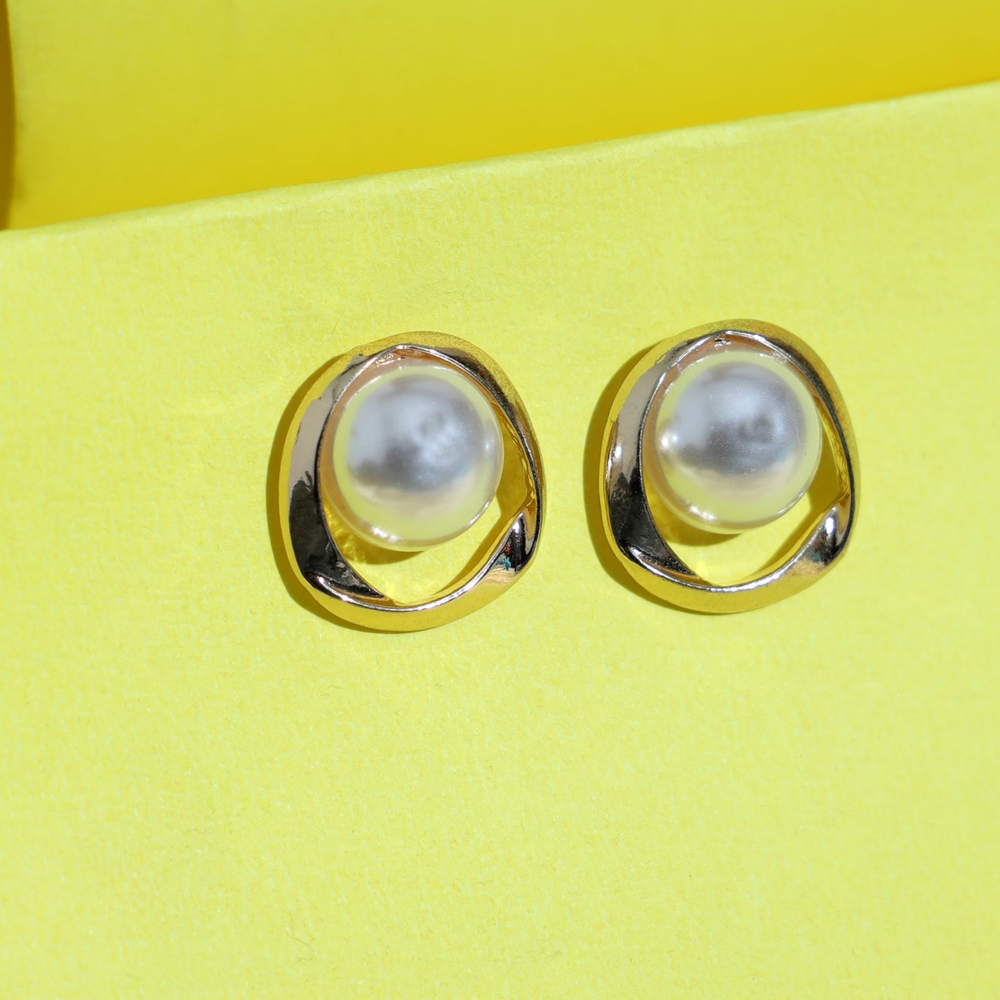 Vintage gold and pearl earrings featuring round white pearls set in open, wavy gold frames capture the timeless elegance of French vintage jewelry, displayed against a bright yellow background.