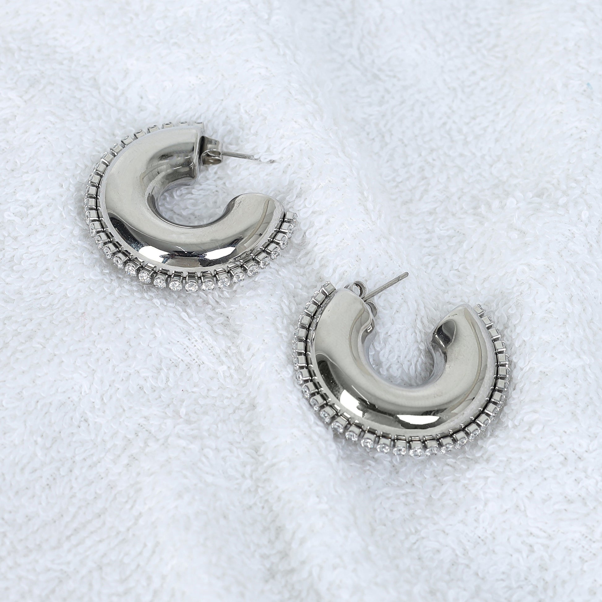 The Half Circle Silver Hoop features a shiny silver finish and a beaded edge design, beautifully showcased on textured white fabric.