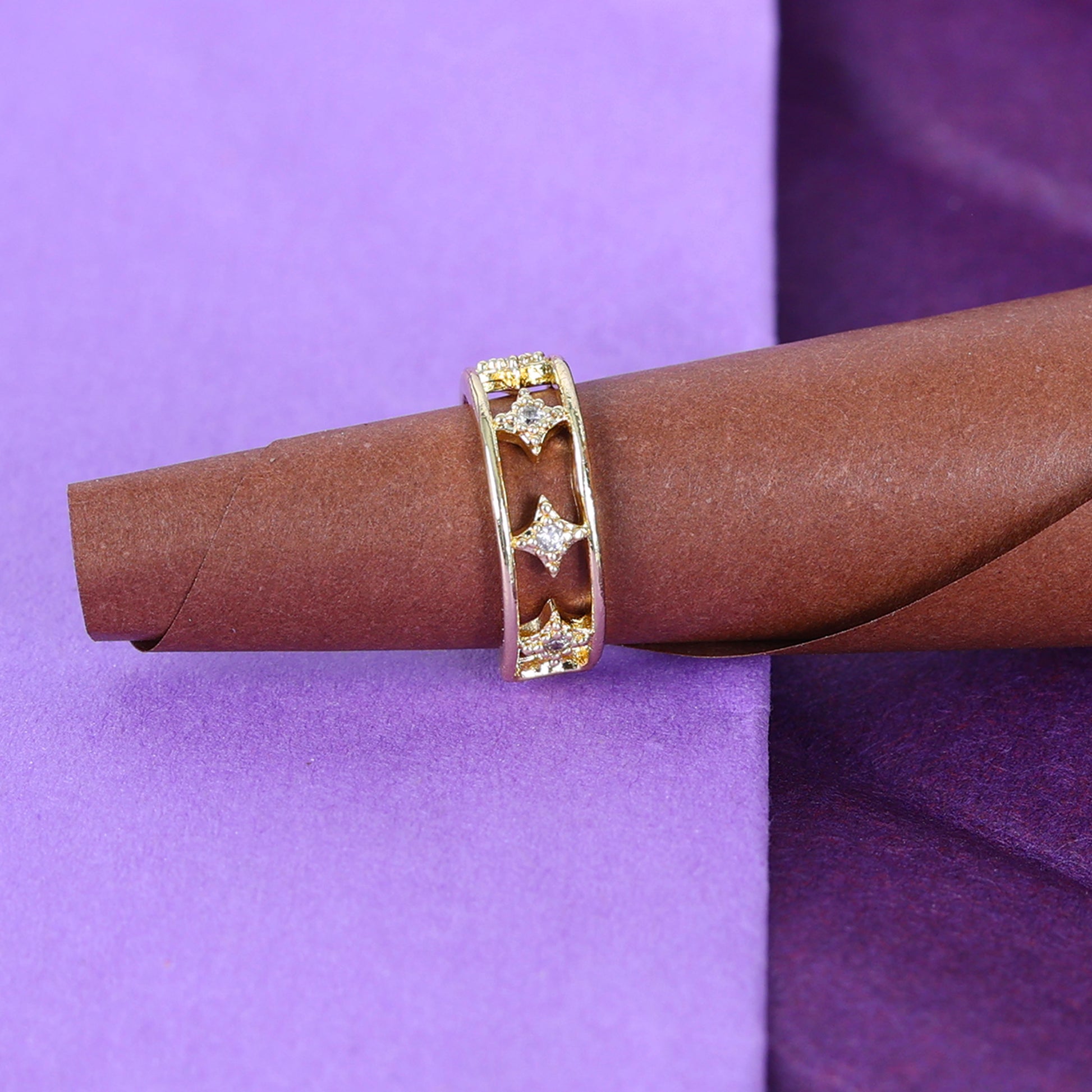 A Small Gold Ear Cuff with a star-shaped cutout and lab-created stones is displayed on a rolled piece of brown paper, set against a purple background.