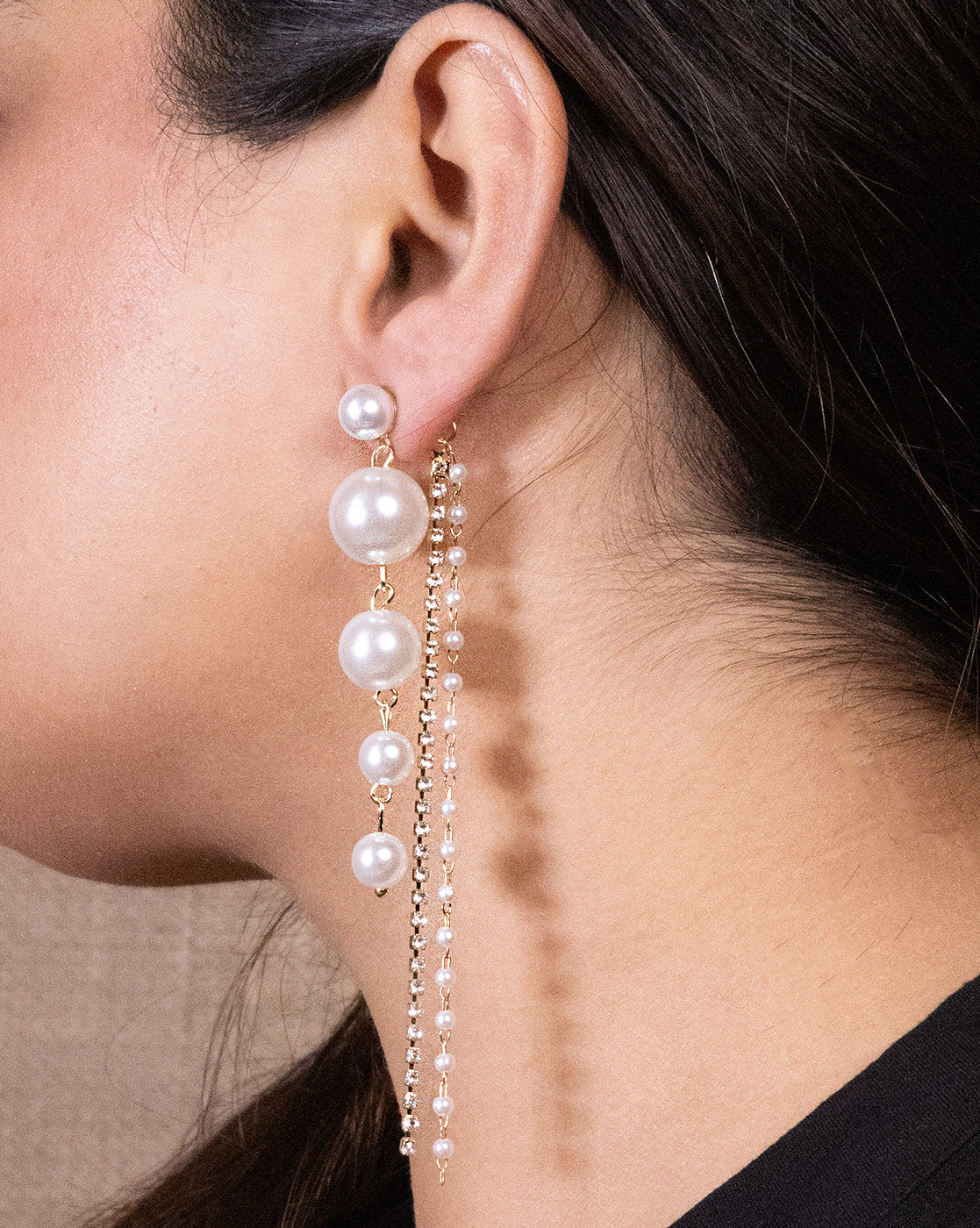 Close-up of a woman's ear wearing Pearl Tassel Earrings—featuring four large pearls in a vertical line and a long gold-plated chain with small pearl accents, set against a neutral background.