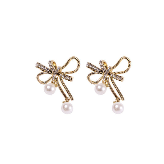 The Bow & Pearl Earrings feature 24K gold plating, bow shapes adorned with rhinestones, and a dangling white pearl on each earring, all inspired by elegant Korean design and shown against a white background.