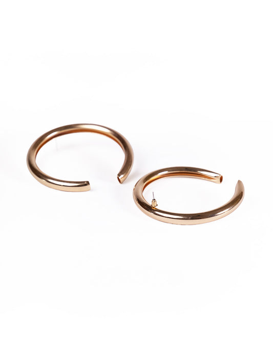Horse shoe shaped earrings, plated in 24K gold with an open-ended design, are laid flat on a white background. One earring reveals the fastening post, highlighting their modern luxury style.