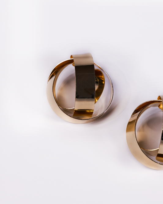 A close-up of the Gold Criss Cross Earrings, featuring modern overlapping gold-toned bands on a white surface—an elegant, affordable luxury jewelry piece.