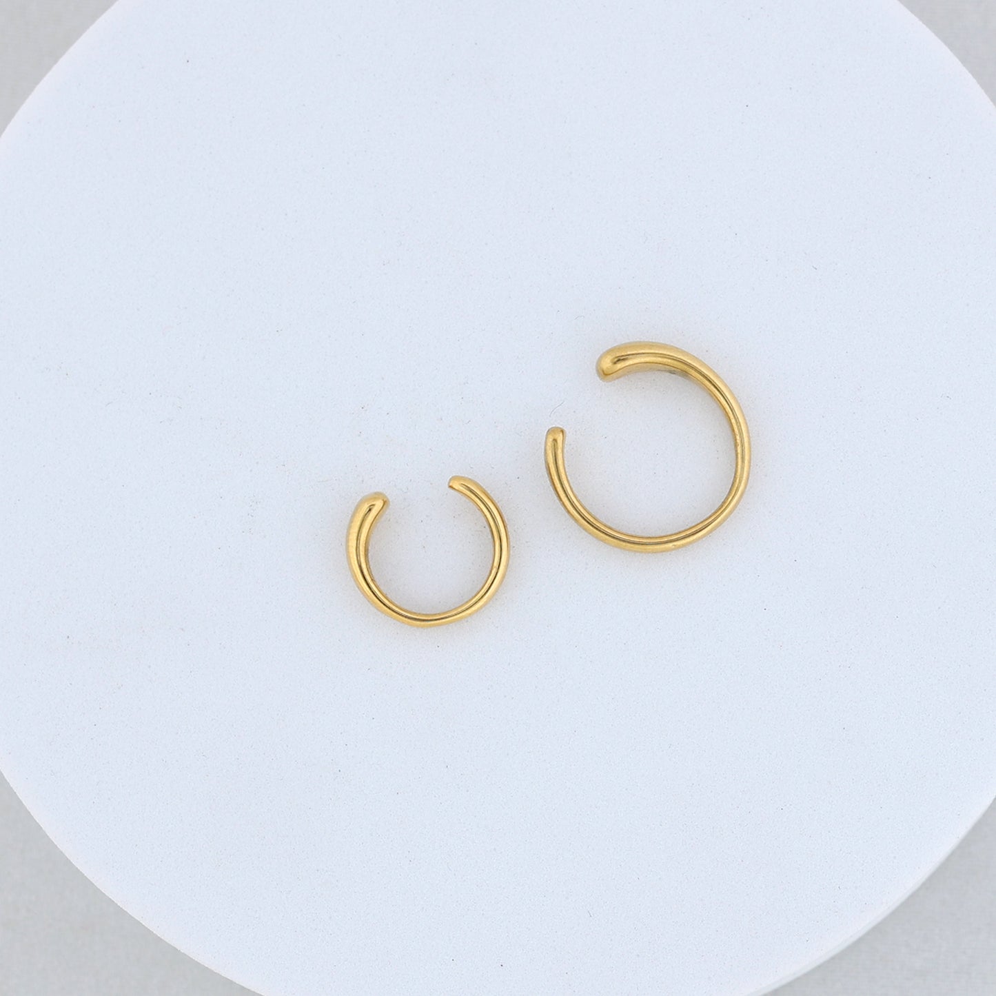 The Gold twin ear cuff features two stylish open hoops of different sizes, displayed side by side on a round white textured surface—a perfect accessory for a modern ear cuffs look.