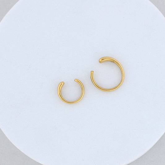 The Gold twin ear cuff features two stylish open hoops of different sizes, displayed side by side on a round white textured surface—a perfect accessory for a modern ear cuffs look.