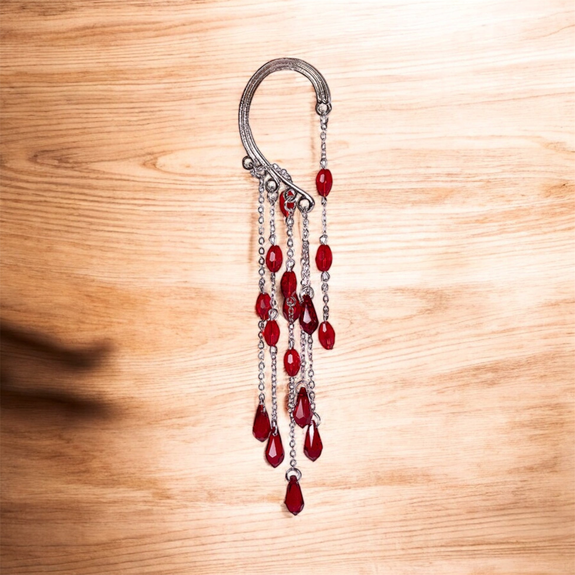 The Red Beads Ear Cuff (left ear) features dangling chains with red teardrop-shaped beads, displayed on a light wooden surface.